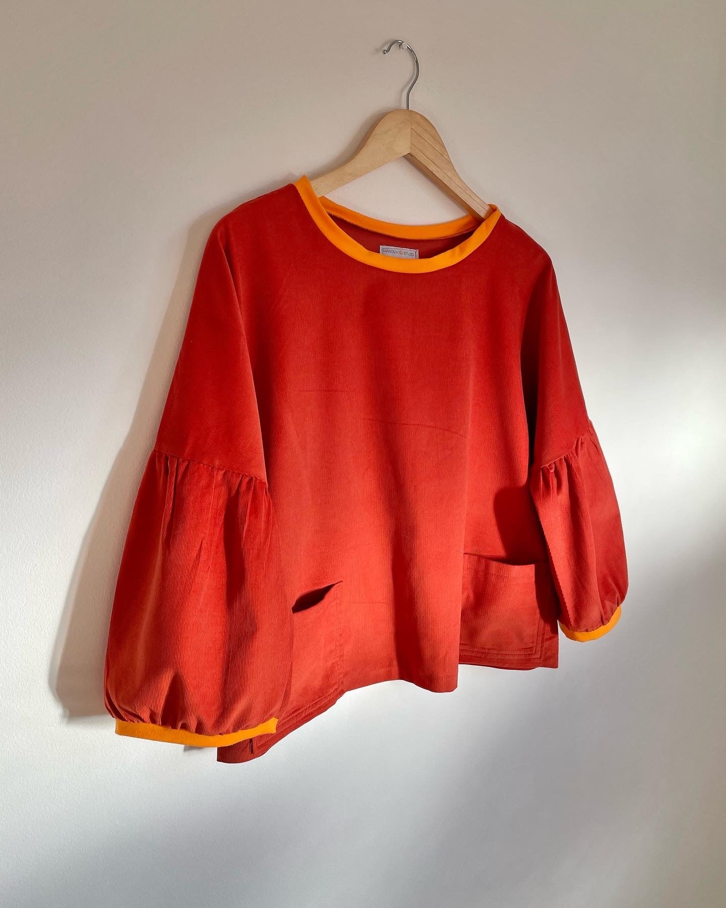 terracotta cord cloud blouse with orange neon trim on a hanger