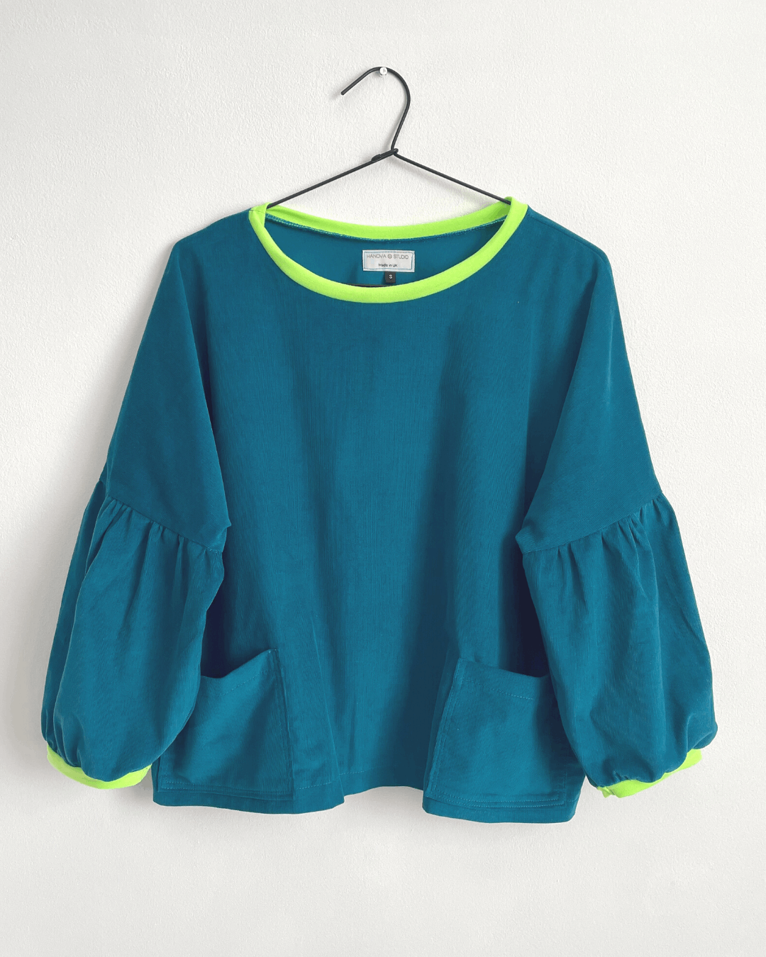 teal cord cloud blouse with neon trim on a hanger