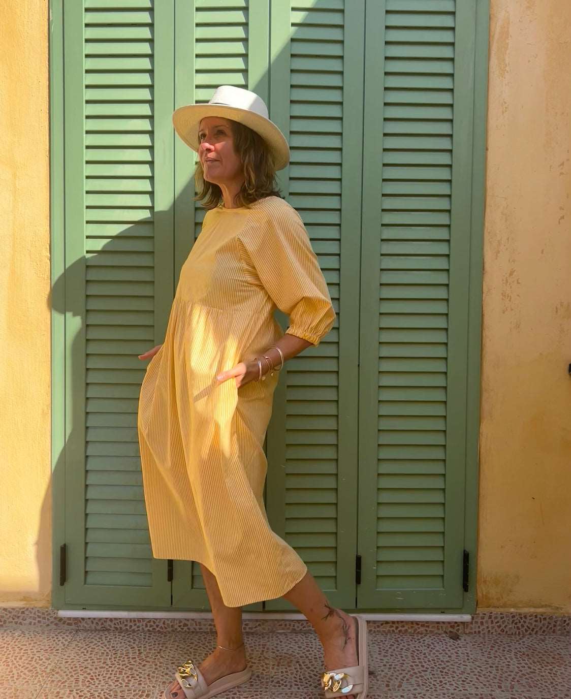 Model wearing lemon stripe dress with pockets wearing a sun hat